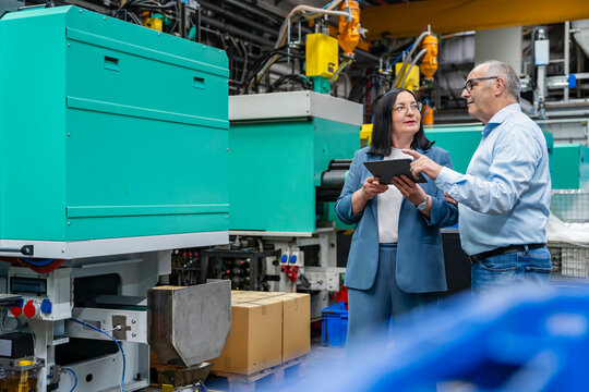 A woman and a man discuss planning on a tablet in a production hall