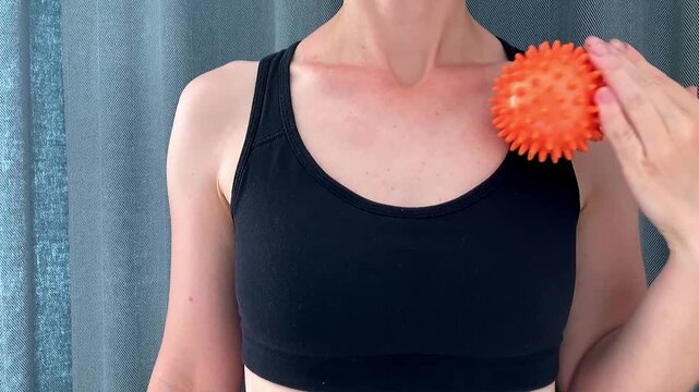 The woman is performing a relaxing self‑massage with an orange massage ball at home to relieve muscle tension, stimulate blood circulation, and restore the body after an active day. Close-up