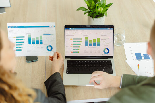 Businesspeople analyze data on a laptop and paper in the office
