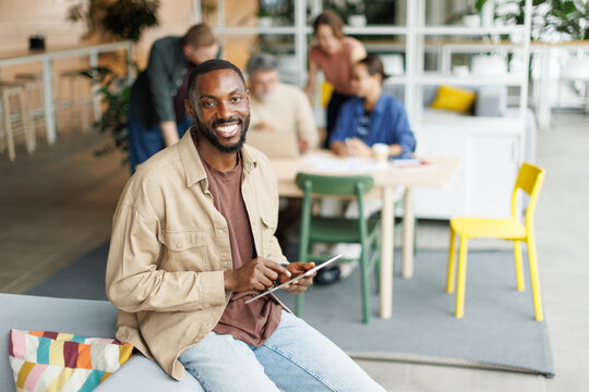 A smiling businessman holds a tablet in an office with colleagues