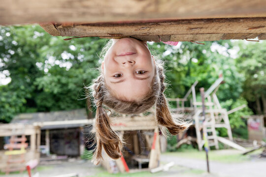 A girl looks at the camera while hanging upside down outdoors