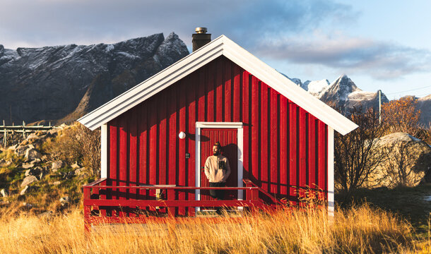 Man with hands in pockets standing on porch of red log cabin