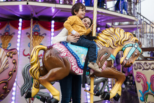 Mother supports her son on a carousel horse