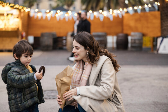 Smiling mother and son enjoy a churro at a winter street market