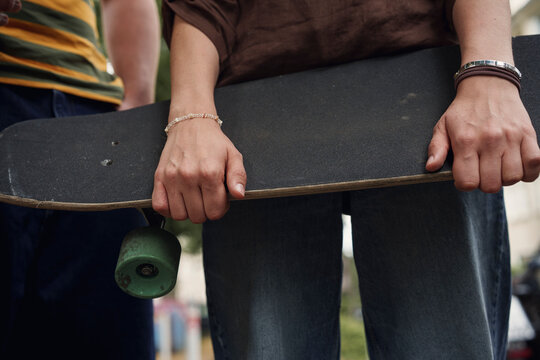 A woman holds a skateboard while standing outdoors with a man