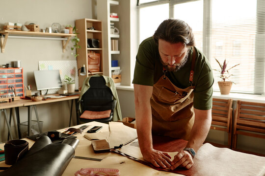 Male artisan working with leather at a table in his workshop