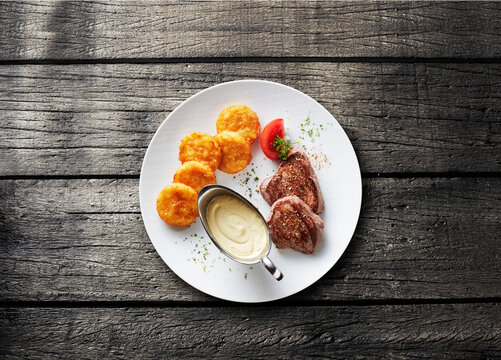 A rustic table holds a plate of grilled steak with rosti and sauce