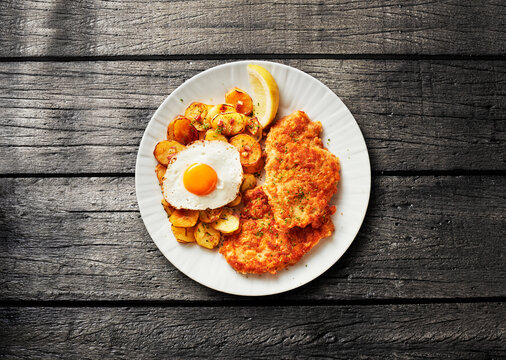 Chicken schnitzel with fried potato and egg lies on a white plate
