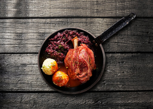 Roasted pork knuckle with red cabbage and dumpling in a pan