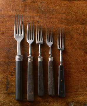 Five vintage forks lie on a scratched wooden table