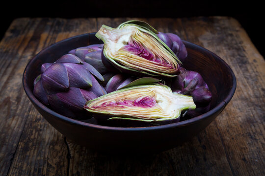 Bowl of purple organic artichokes on dark wood