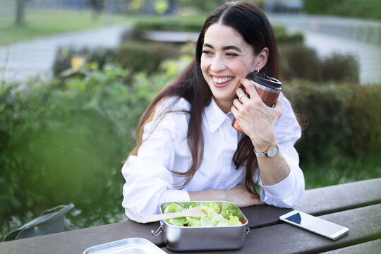 Smiling businesswoman enjoys healthy lunch and coffee break outdoors