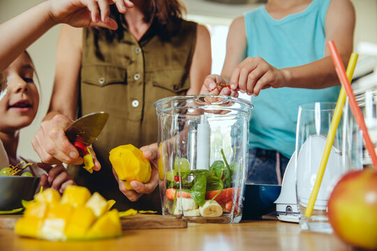 Mother and children putting fruit into a smoothie blender