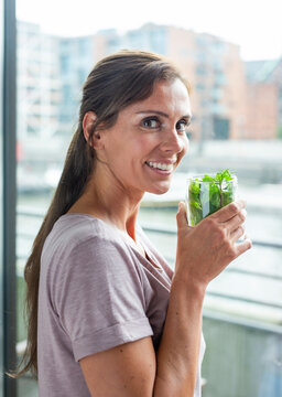 Smiling woman holds a glass of fresh mint tea indoors