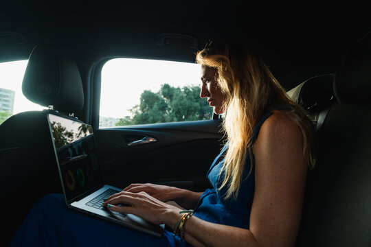 Businesswoman works on a laptop in the back seat of a car