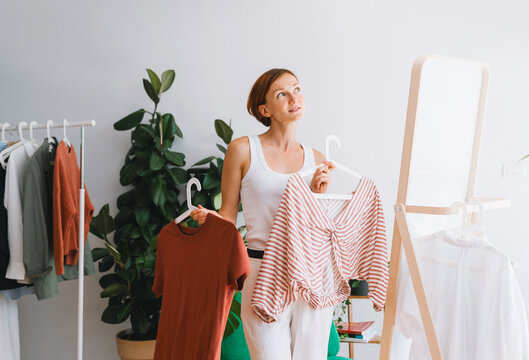 Thoughtful woman choosing a shirt indoors for wardrobe decluttering