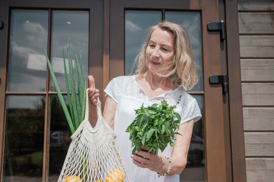 Woman holds a mesh bag with healthy food and fresh herb outdoors