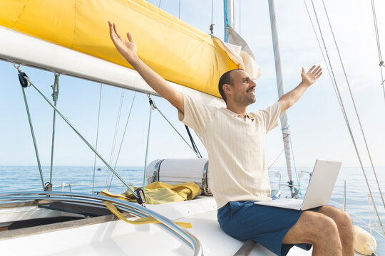 Happy man celebrates remote work success on a sailboat in Spain