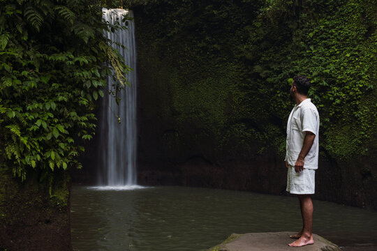 A male tourist watches a waterfall in the lush jungle of Bali