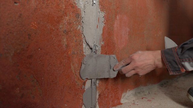 Construction worker's hand applying grey plaster to a wall joint with a trowel during renovation