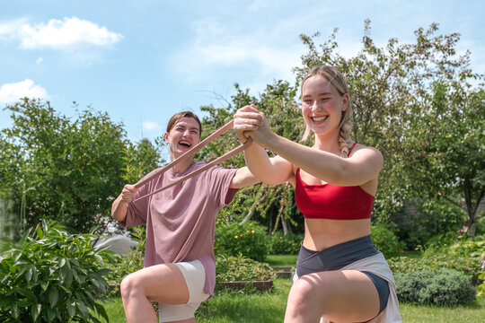 Female friends exercise with a resistance band in a sunny garden