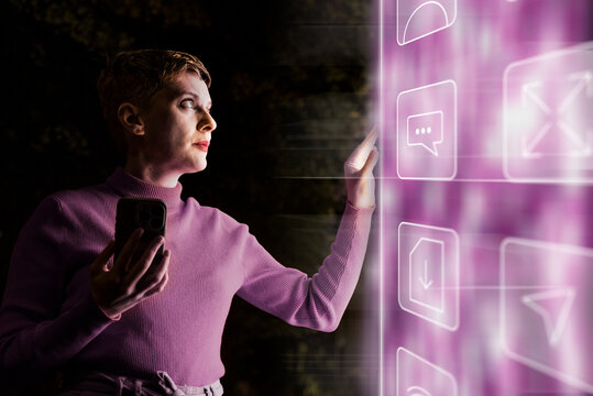 Woman touches futuristic digital screen holding smartphone at night