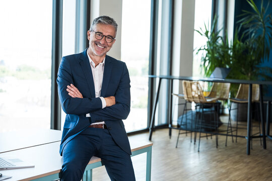 Confident businessman sits on a desk in a modern office