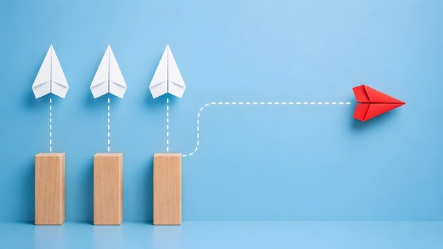 Red paper airplane flying forward while white ones are grounded on wooden pillars demonstrating innovation, breaking the mold, and taking initiative.
