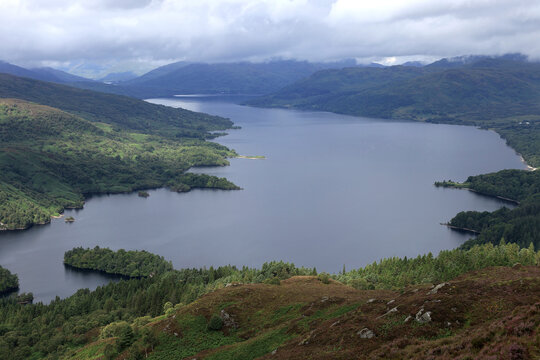 Aerial photo with a view of Loch Katrine lake and the surrounding mountains partially covered by clouds from the top of Ben A'an mountain in Scotland, United Kingdom