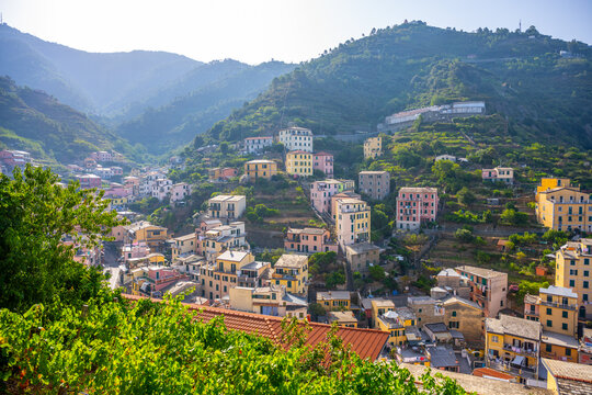 Riomaggiore Village in Cinque Terre shows colorful houses on hills. The scene captures the village's layout and surrounding mountains under bright sunlight.