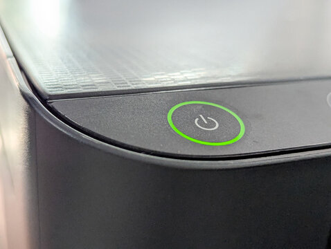 Detailed close-up of an illuminated green LED power button on a textured black electronic device.