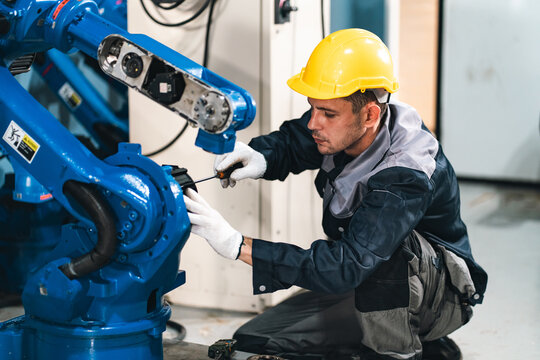 Industrial worker repairs robotic arm in factory with protective helmet and gloves, demonstrating careful maintenance and technical expertise during equipment service