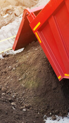 Red dump truck raising bed, discharging loose earth material onto ground, construction site operations, heavy equipment work, building industry development, vertical photo © HENADZY