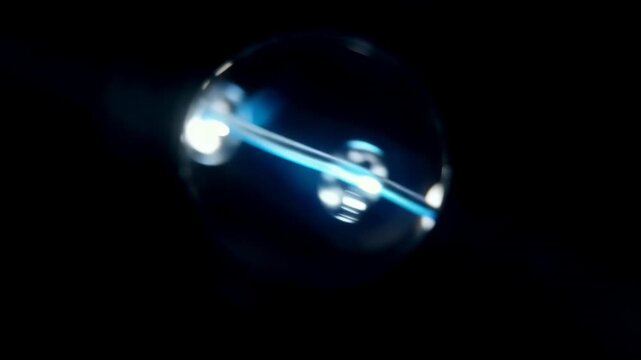 Close-up view of a glass sphere reflecting blue light beams, showcasing the continuous flow of light through the transparent surface in a dark environment
