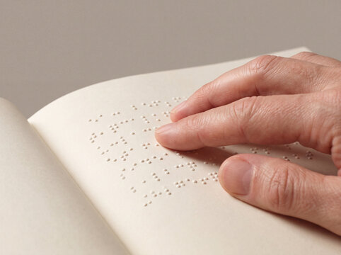 Fingers read embossed Braille dots across a tactile white book page.