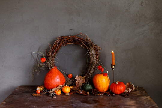 Autumn still life. Colorful pumpkins, autumn leaves, acorns, stylish wreath and candle on rustic wooden table on moody dark background. Happy Thanksgiving and harvest. Fall season greeting card