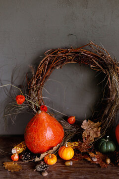 Pumpkins, autumn leaves, nuts, berries, rustic wreath on old wooden table on moody dark background. Happy Thanksgiving. Atmospheric autumn still life. Harvest. Fall season banner