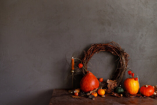 Pumpkins, autumn leaves, nuts, berries, rustic wreath and candle on old wooden table on moody dark background. Happy Thanksgiving. Atmospheric autumn still life. Harvest. Fall season banner