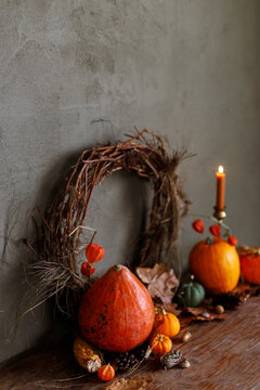 Autumn still life. Colorful pumpkins, autumn leaves, acorns, stylish wreath and candle on rustic wooden table on moody dark background. Happy Thanksgiving and harvest. Fall season greeting card