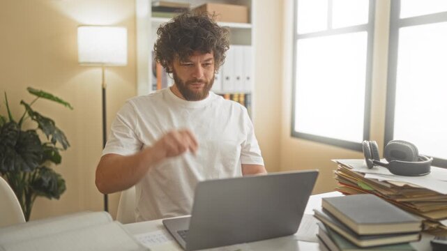 Man at study desk with laptop and stacked books, hands behind head stretching and leaning back in building; relaxation study break.