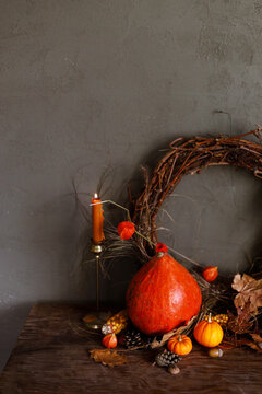 Pumpkins, autumn leaves, nuts, berries, rustic wreath and candle on old wooden table on moody dark background. Happy Thanksgiving. Atmospheric autumn still life. Harvest. Fall season banner