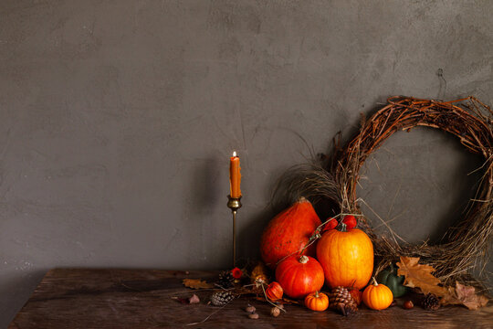 Pumpkins, autumn leaves, nuts, berries, rustic wreath and candle on old wooden table on moody dark background. Happy Thanksgiving. Atmospheric autumn still life. Harvest. Fall season banner