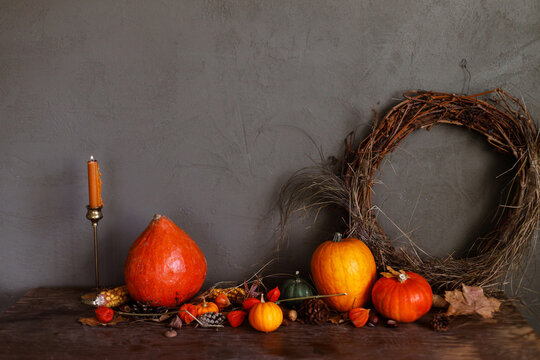 Pumpkins, autumn leaves, nuts, berries, rustic wreath and candle on old wooden table on moody dark background. Happy Thanksgiving. Atmospheric autumn still life. Harvest. Fall season banner