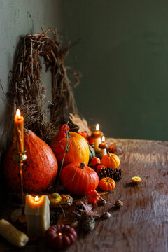 Pumpkins, autumn leaves, nuts, berries, rustic wreath and candle on old wooden table on moody dark background. Happy Thanksgiving. Atmospheric autumn still life. Harvest. Fall season banner