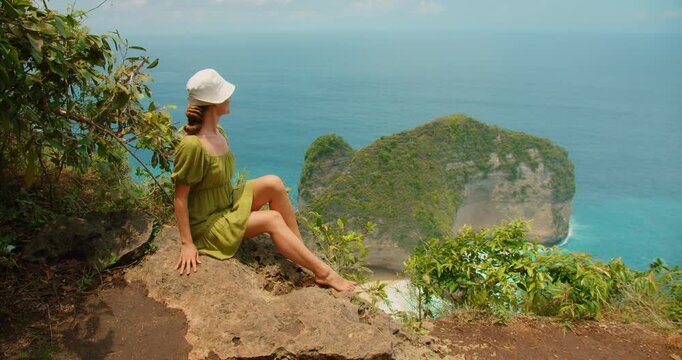 Woman sitting on cliff edge enjoying peaceful ocean view at Nusa Penida Bali