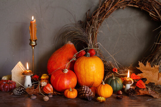 Happy Thanksgiving. Pumpkins, autumn leaves, nuts, rustic wreath, candle on old wooden table on moody background. Atmospheric autumn still life with copy space. Fall season banner or card