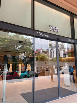 A modern Zara store entrance showcases sleek glass doors and a minimalist design. The store's name is prominently displayed above. Surrounding elements suggest an urban setting.