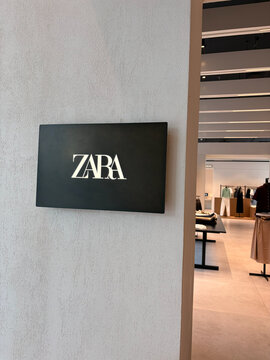 A sleek sign displays the Zara logo in a modern retail store. The interior features neutral colors and contemporary design elements, highlighting a stylish shopping environment.