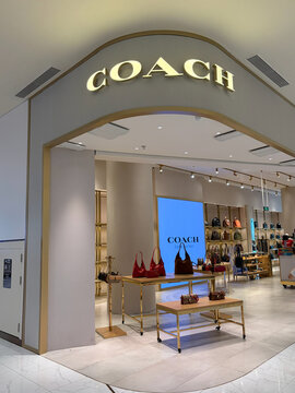 An upscale Coach retail store entrance features a modern design. The storefront displays stylish merchandise and a large logo overhead. The interior showcases various accessories.