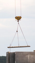 vertical photo of crane hook lifting large concrete panel for high-rise building construction against light sky, industrial development progress of urban infrastructure © HENADZY